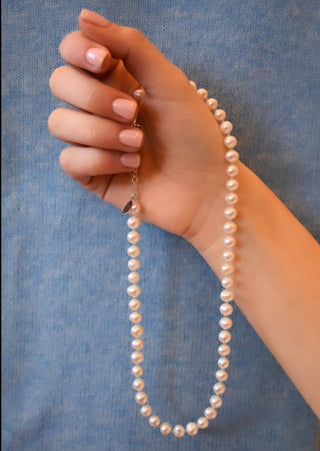 White freshwater pearl necklace in hand with blue cashmere