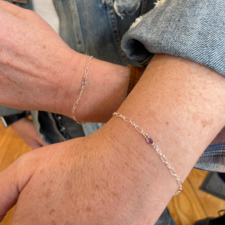 Close-up of two wrists wearing silver permanent bracelets with a blurred background