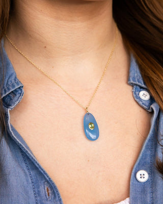 Person wearing a necklace with a blue pendant and gold chain.