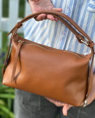 Brown leather handbag held by a person outdoors