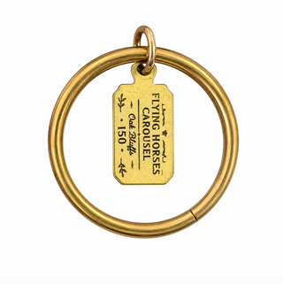 A vintage brass ring with a hanging tag engraved with 'FLYING HORSES CAROUSEL - Oak Bluffs - 150'.