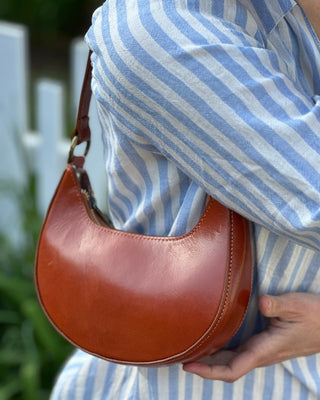 Brown leather handbag held by a person wearing a blue and white striped shirt.