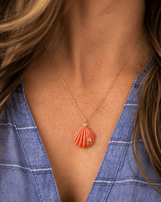 Necklace with a coral-colored shell pendant worn by a person in a blue shirt.