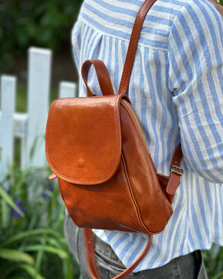 Brown leather backpack worn by a person in a striped shirt outdoors.