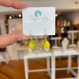 Yellow lemon-shaped earrings on a card held by a hand with a blurred indoor background