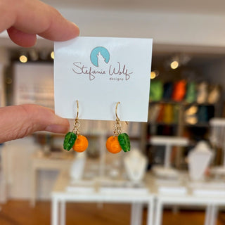 Hand holding a card with orange fruit  earrings on a blurred indoor background