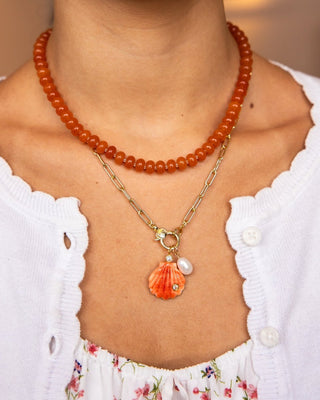 Close-up of a person wearing two necklaces, one with orange beads and the other with a shell pendant.