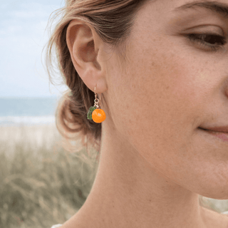 Orange fruit earrings on gold on a woman at the beach
