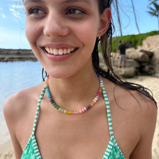 Woman wearing a green bikini with floral patterns and colorful straps, standing outdoors.