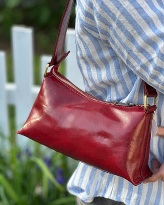 Red leather handbag held by a person wearing a striped shirt outdoors.