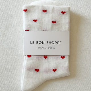 White socks with red hearts and 'Le Bon Shoppe' packaging on a light background