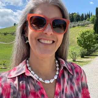 Woman wearing sunglasses baroque pearls, and a colorful dress with a scenic background in Tuscany