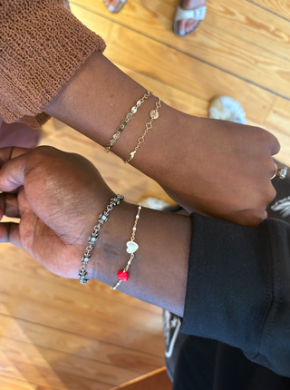 Two wrists with gold and silver bracelets on a wooden surface