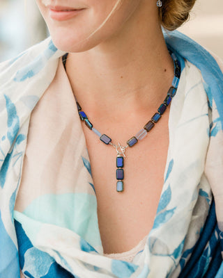 Necklace with blue beads worn by a woman in a light-colored scarf with blue patterns.