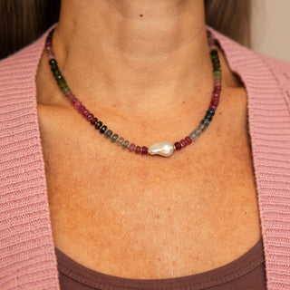 Necklace with multicolored tourmaline beads and a baroque pearl pendant on a person wearing a pink top.