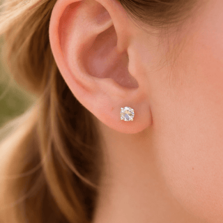 Close-up of an ear wearing a white topaz stud earring with blurred hair and skin in the background