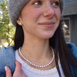 White freshwater pearl necklace and stud earring set on woman in sweater with hat